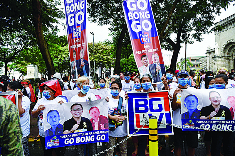 In this photo taken on November 15, 2021, supporters of Philippine senator and presidential candidate Bong Go (pictured on placards) hold a rally in front of the commission on elections office in Manila, on the final day for candidates to file for the presidential and vice presidential races in 2022. (Photo by TED ALJIBE / AFP)